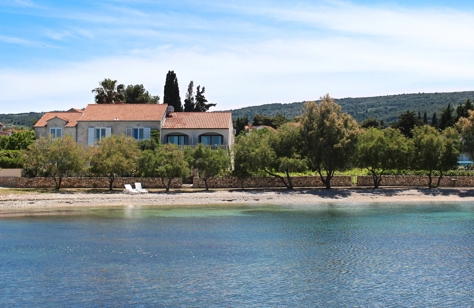Villa Mirca seen from the sea — a stone villa with red roofs above its private beach, Brač Island, Croatia