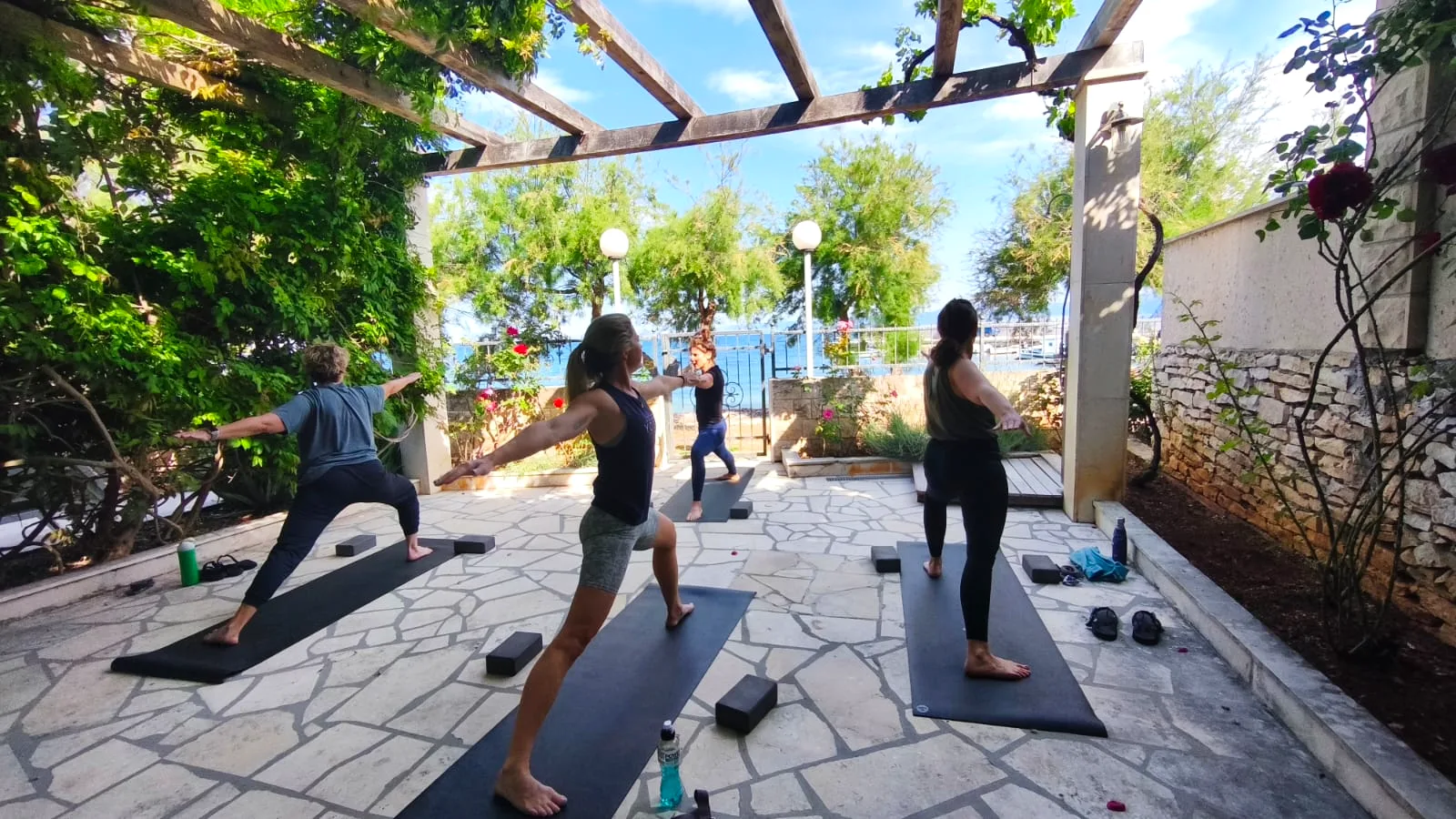 Group practising yoga on mats under the vine-covered pergola terrace facing the sea at Villa Mirca, Brač Island