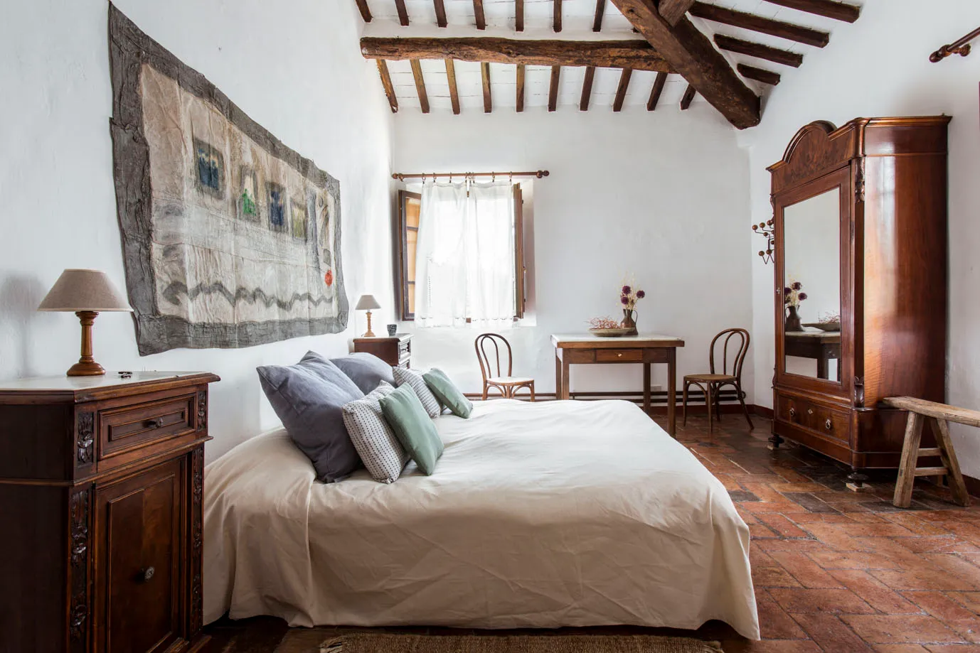 Double bedroom with carved headboard and rugs at Ebbio Tuscany, Italy