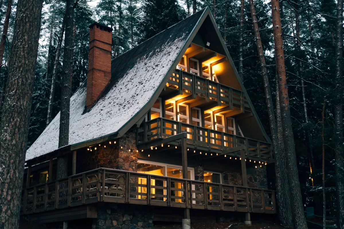 A-frame lodge lit up at twilight among pine trees at Šiaurys Resort, Lithuania