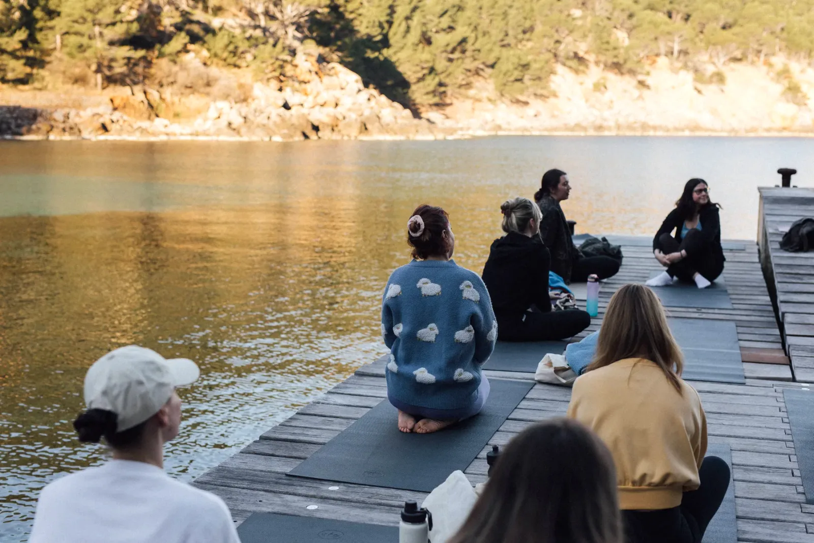 Retreat group practicing yoga at golden hour on the dock, Mallorca